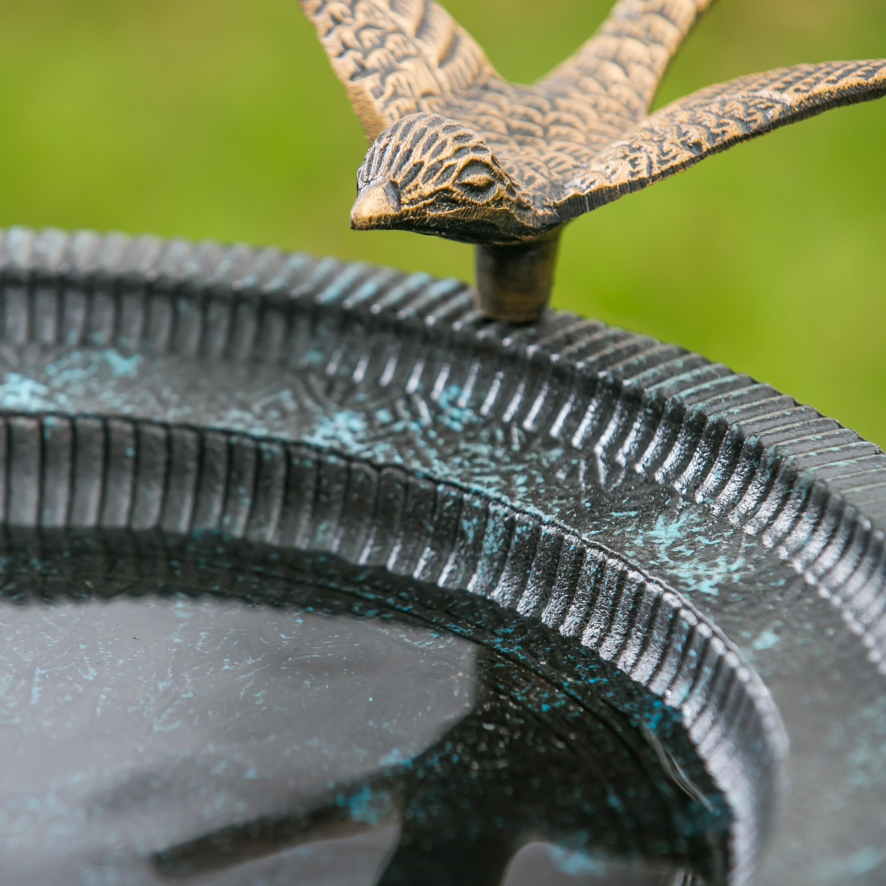 Close-up of bronzed songbird figure perched on the birdbath basin rim