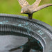 Close-up of bronzed songbird figure perched on the birdbath basin rim