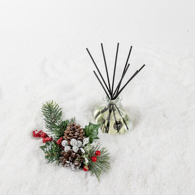 Comfort & Joy Reed Diffuser with black reeds on snowy pinecones and pine branches