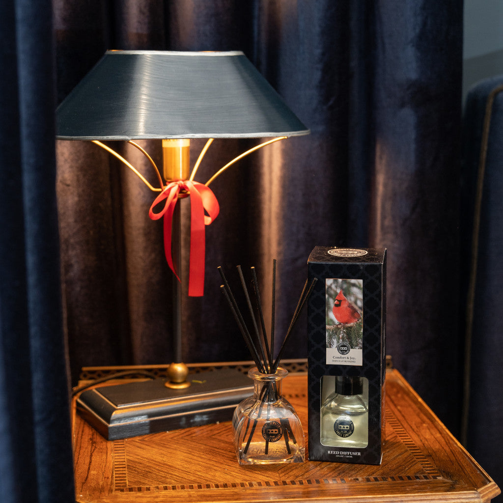 Comfort & Joy Reed Diffuser on a wooden side table with lamp and blue curtains
